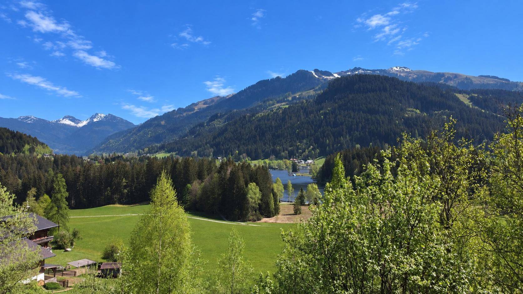 Weitläufige Landschaft mit See, Wäldern und Bergen unter strahlend blauem Himmel.