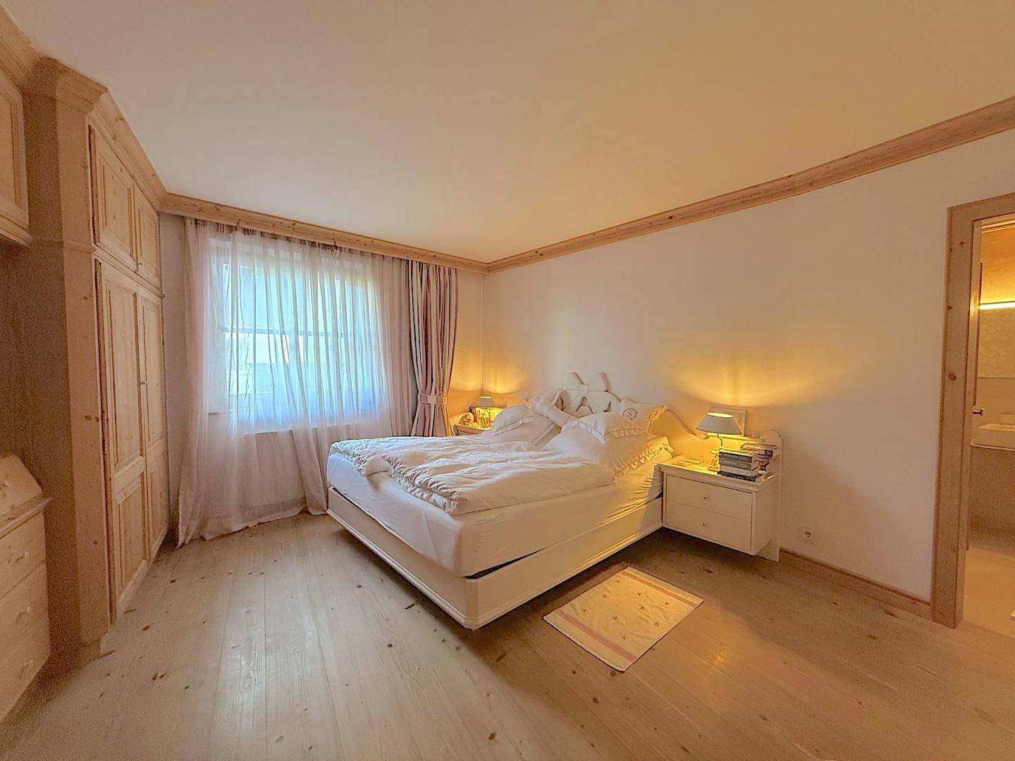 Helles Schlafzimmer mit Doppelbett, Einbauschränken aus Holz und Fenster mit Vorhängen.