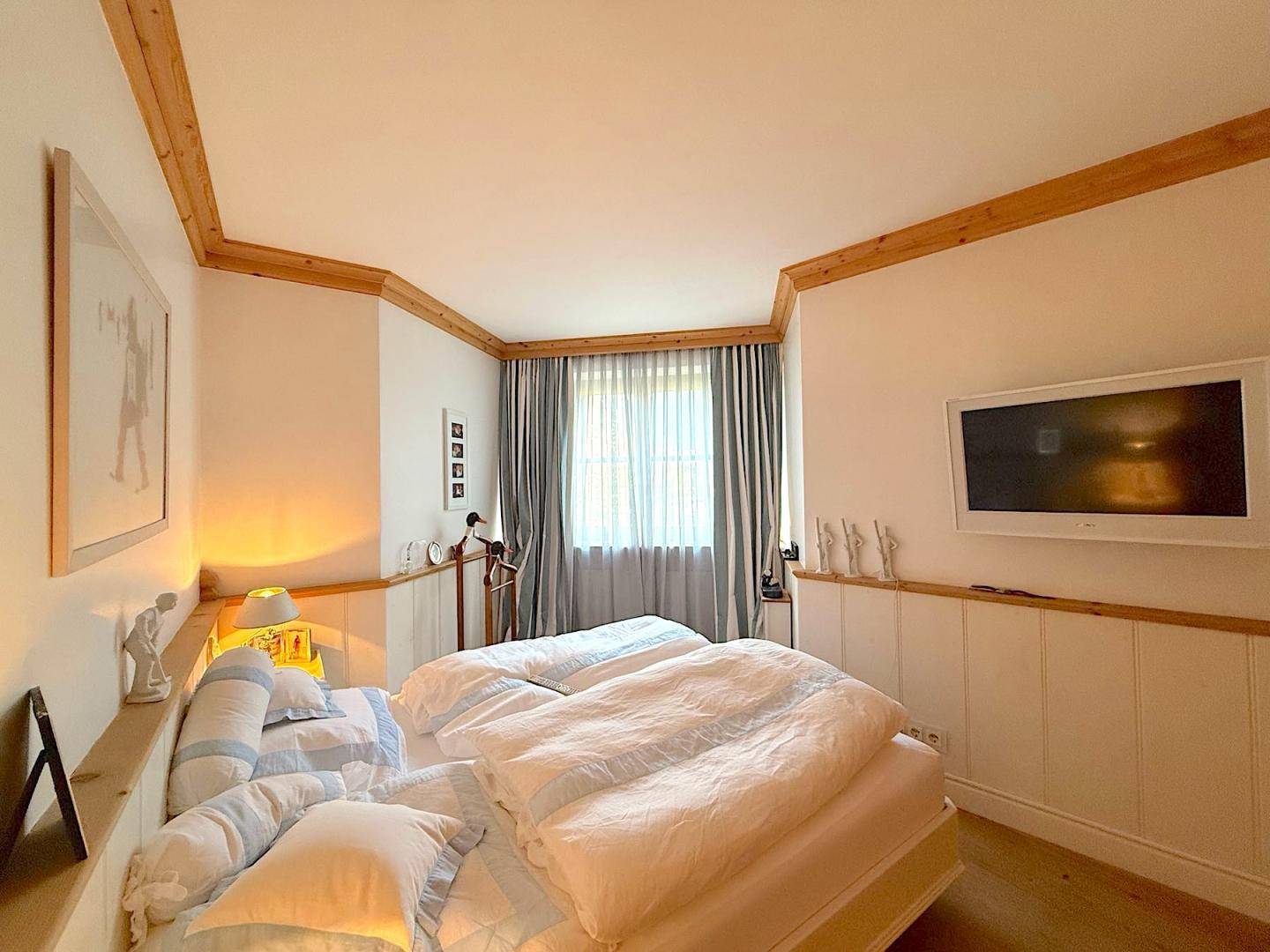 Gemütliches Schlafzimmer mit Doppelbett, Wandfernseher und Holzvertäfelung im unteren Bereich.