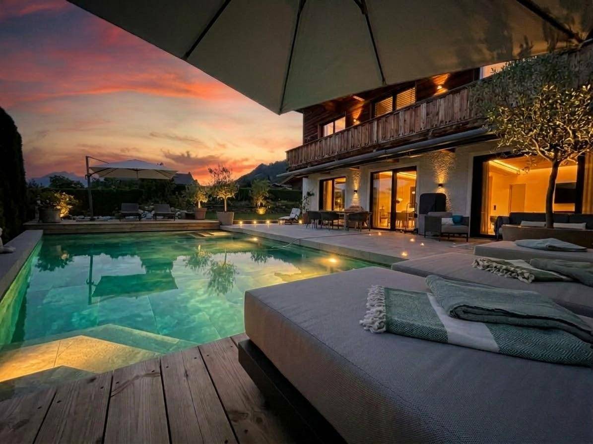 Stilvolle Terrasse mit Pool und bequemen Liegen, umgeben von der malerischen Berglandschaft bei Sonnenuntergang.