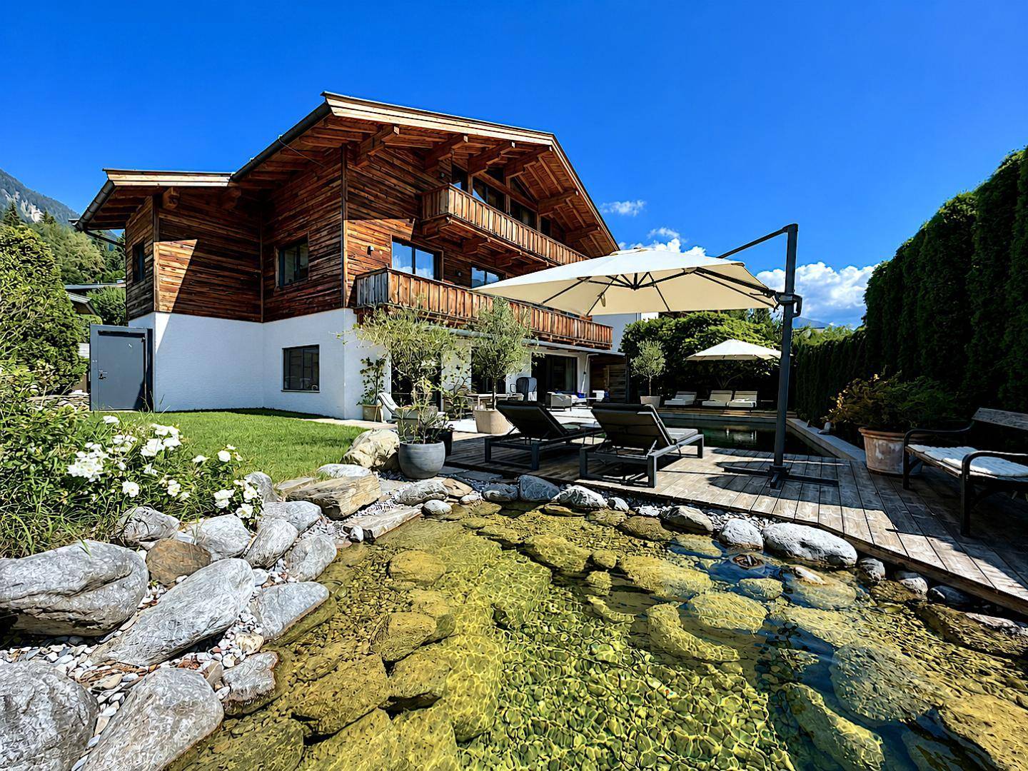 Charmantes Chalet mit großem Garten, Naturteich und sonniger Terrasse, umgeben von grüner Landschaft.
