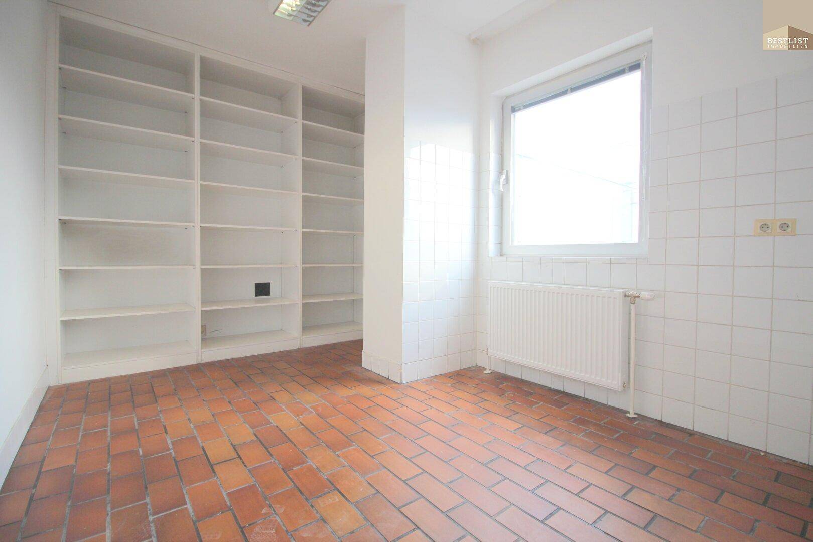 Raum mit Terrakottafliesenboden, weißen Wandfliesen und großen, eingebauten Regalen.