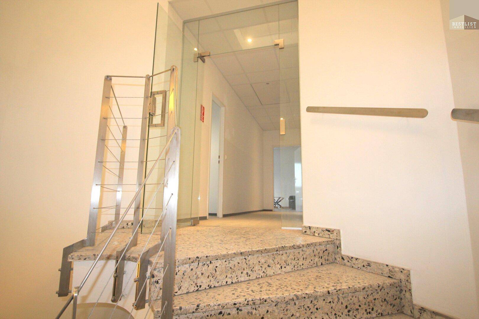 Eingangsbereich mit einer Treppe aus Terrazzo und Edelstahlgeländer, die zu einem Flur führt.