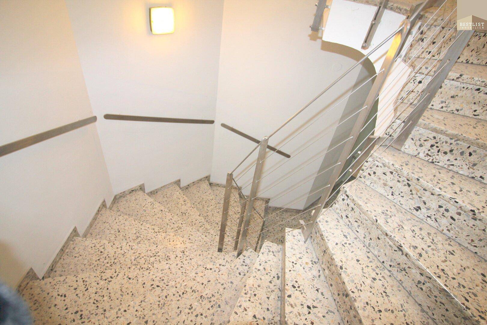 Blick von oben auf eine Wendeltreppe mit Terrazzostufen und modernem Edelstahlgeländer.