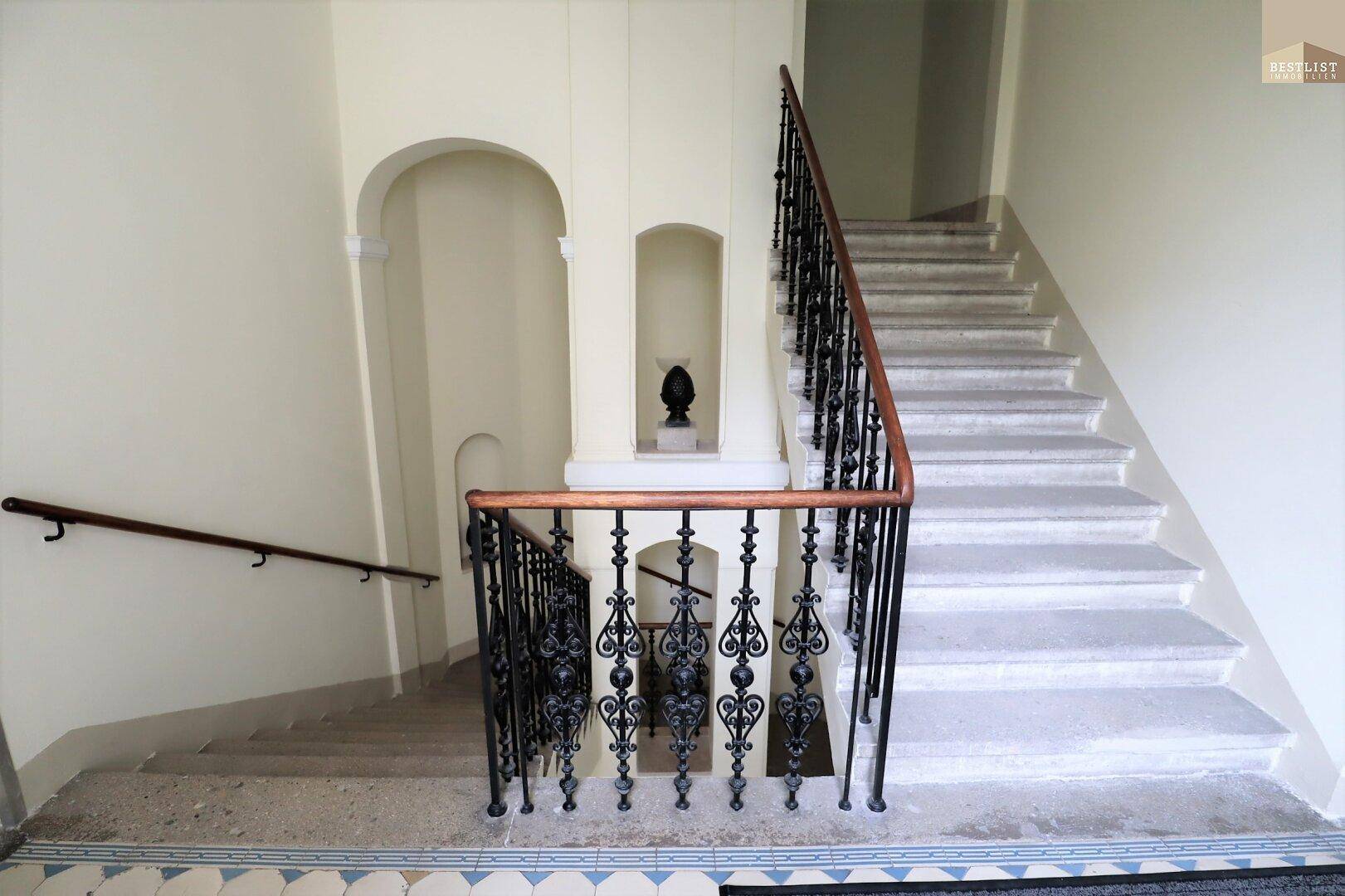 Elegantes Treppenhaus mit schmiedeeisernem Geländer und Stein- oder Terrazzostufen in einem Altbau.