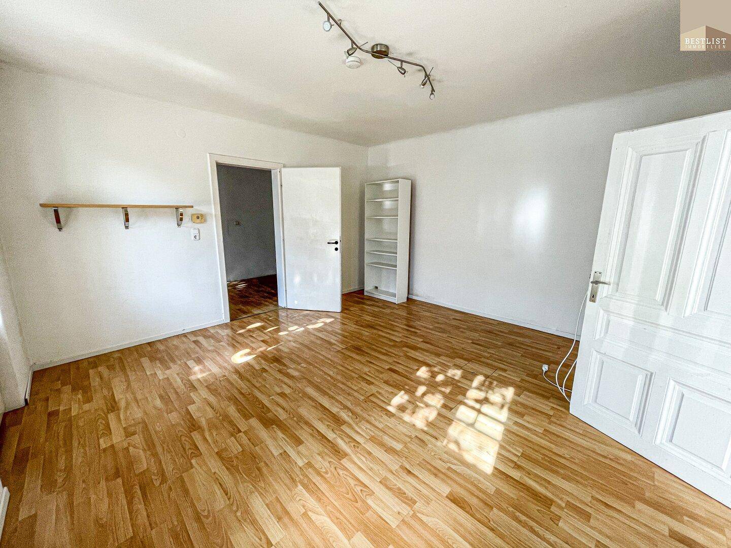 Geräumiger Raum mit Holzboden und zwei Türen, bietet vielseitige Nutzungsmöglichkeiten und Helligkeit.