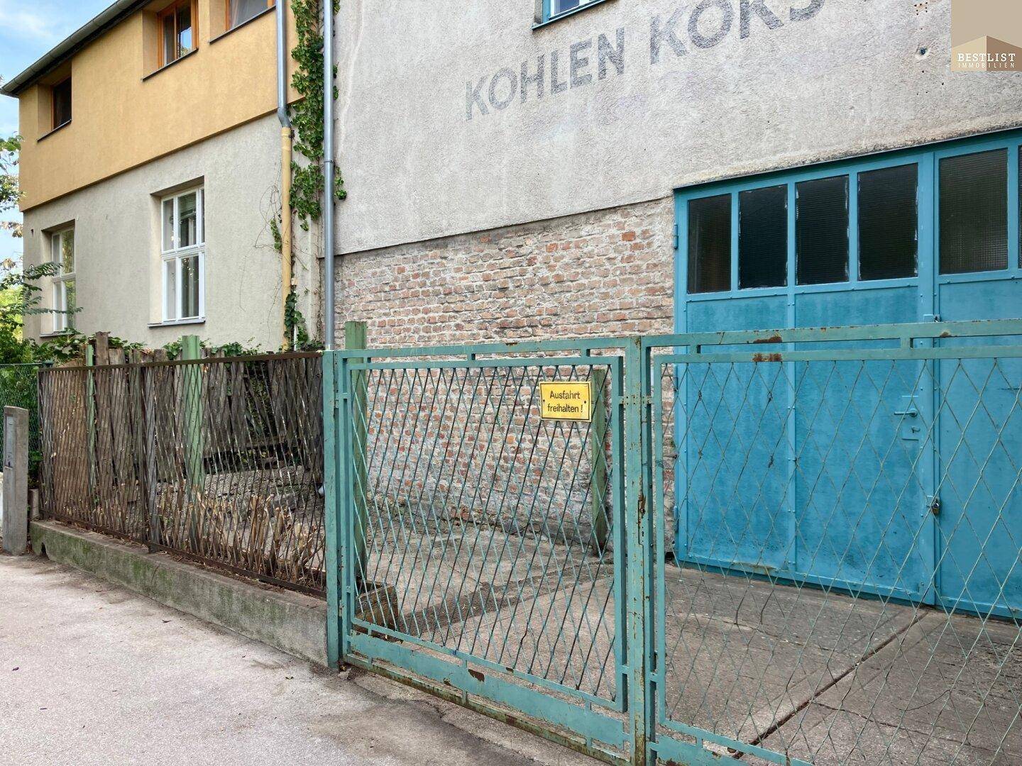 Außenansicht eines Gebäudes mit blauen Toren und einem Zaun, mit altem Schriftzug an der Wand.
