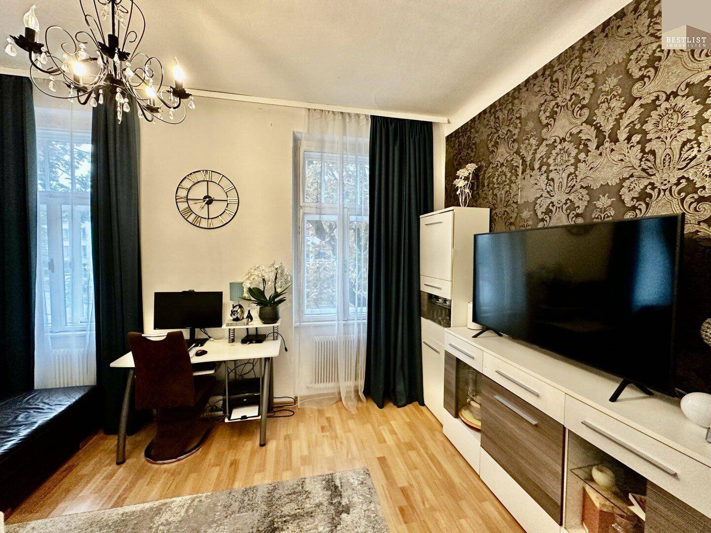 Modern eingerichtetes Wohnzimmer mit Fernseher, dunklen Vorhängen und dekorativer Tapete an einer Wand.
