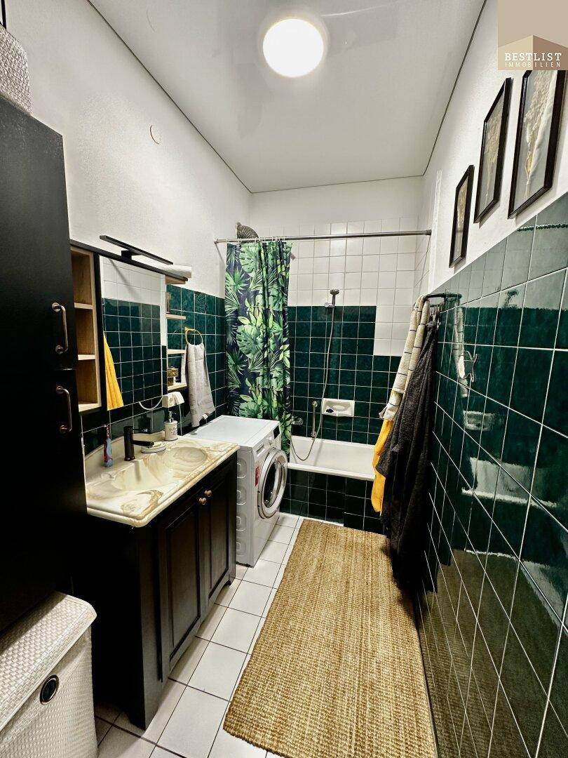 Modernisiertes Badezimmer mit grünen Fliesen, Badewanne und Waschmaschine, funktional und hell.