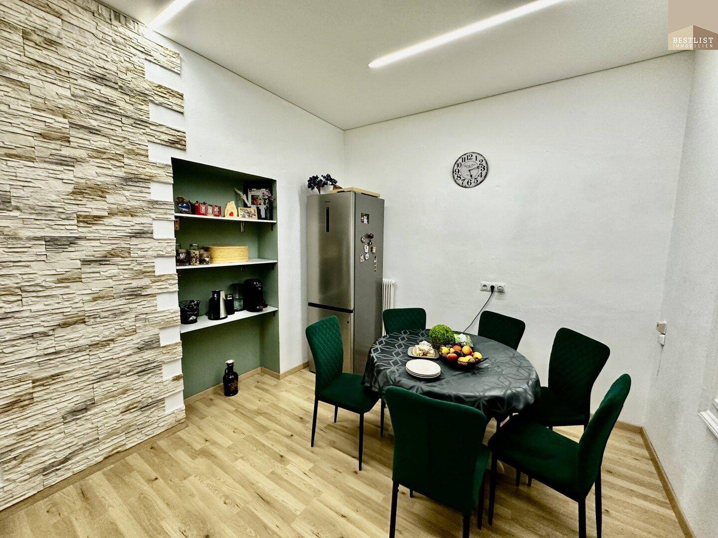 Essbereich mit dekorativer Steinfassade, grünem Mobiliar und Kühlschrank, ideal für gemeinsame Mahlzeiten.