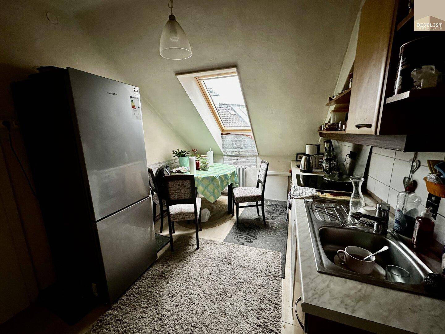 Dachgeschossküche mit Schräge, Dachfenster und Essbereich, funktional eingerichtet und hell.