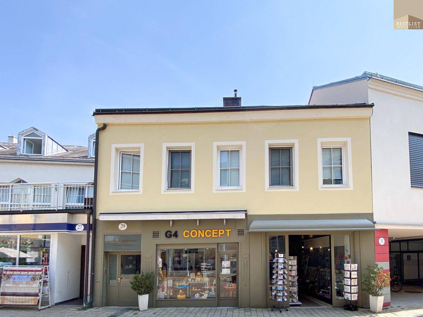 Gelbe Fassade eines Geschäftsgebäudes mit Schaufenstern und Markisen unter blauem Himmel.
