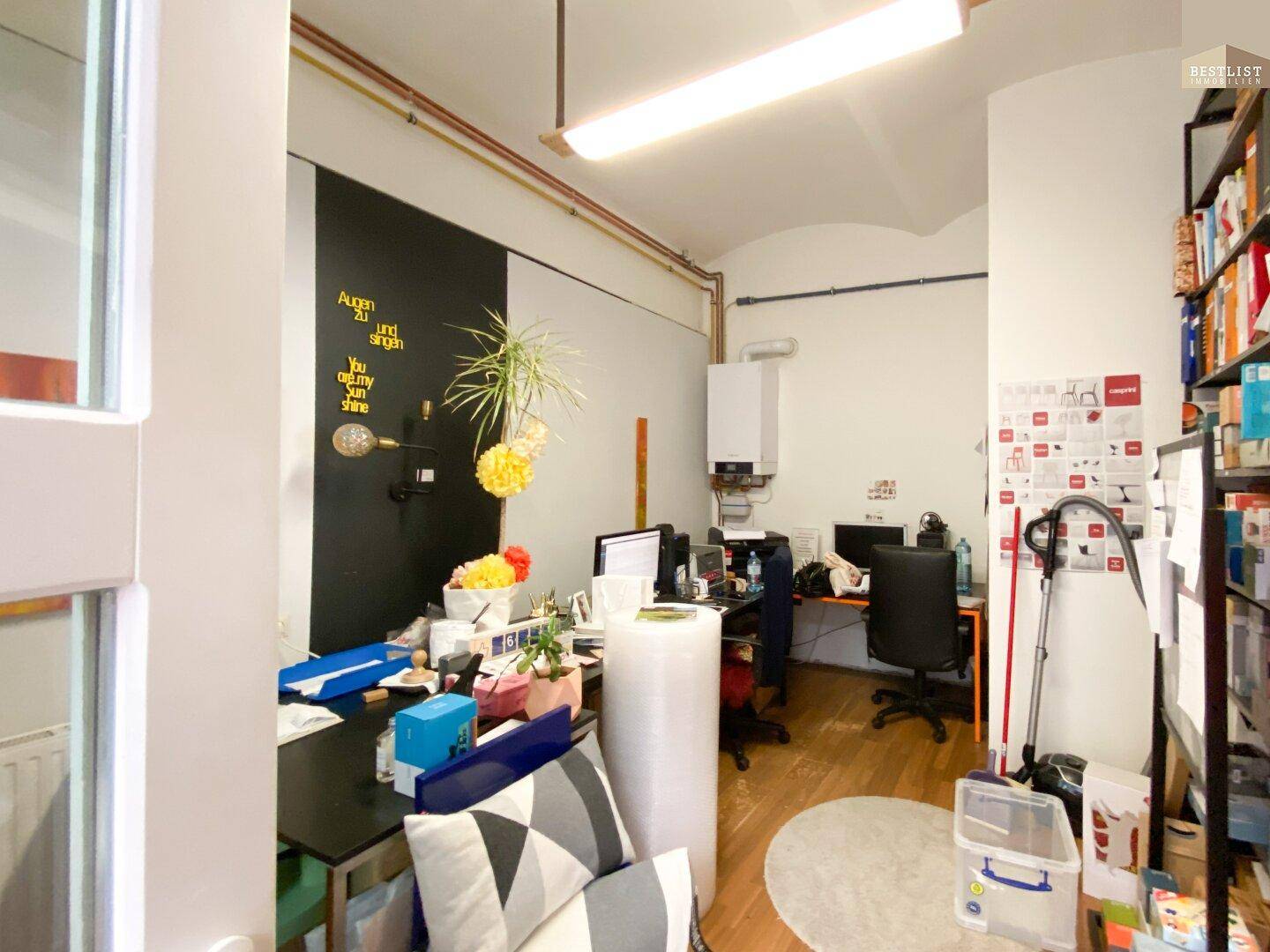 Kleines Büro mit Schreibtischen, Computern und einem Wandheizkessel.