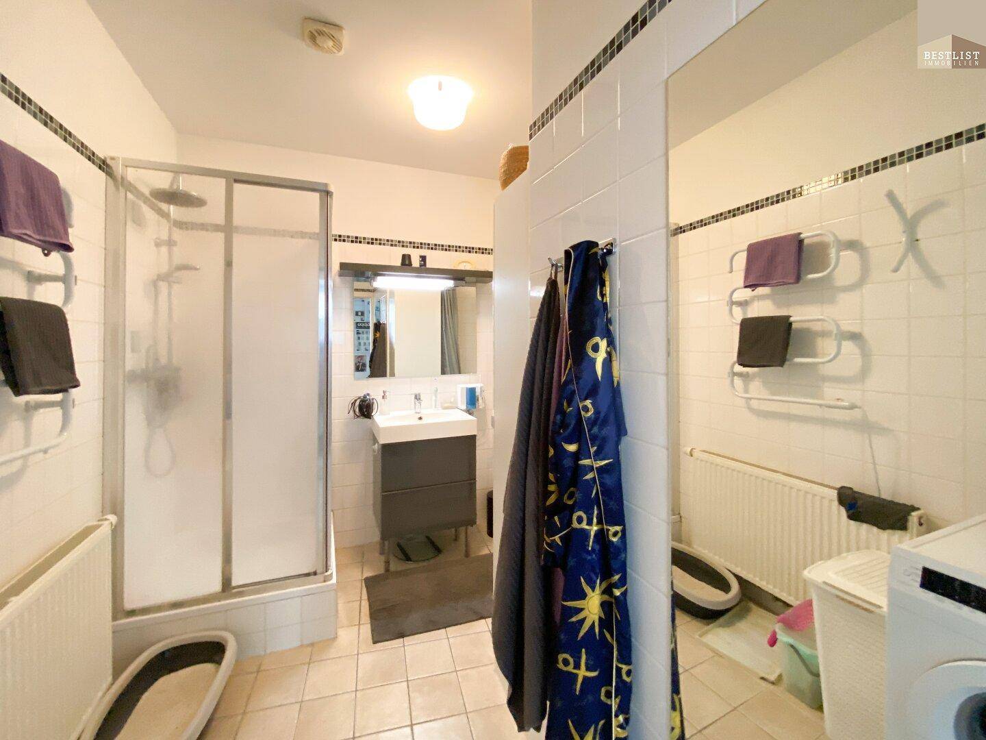Badezimmer mit Duschkabine, Waschbecken und Waschmaschine.