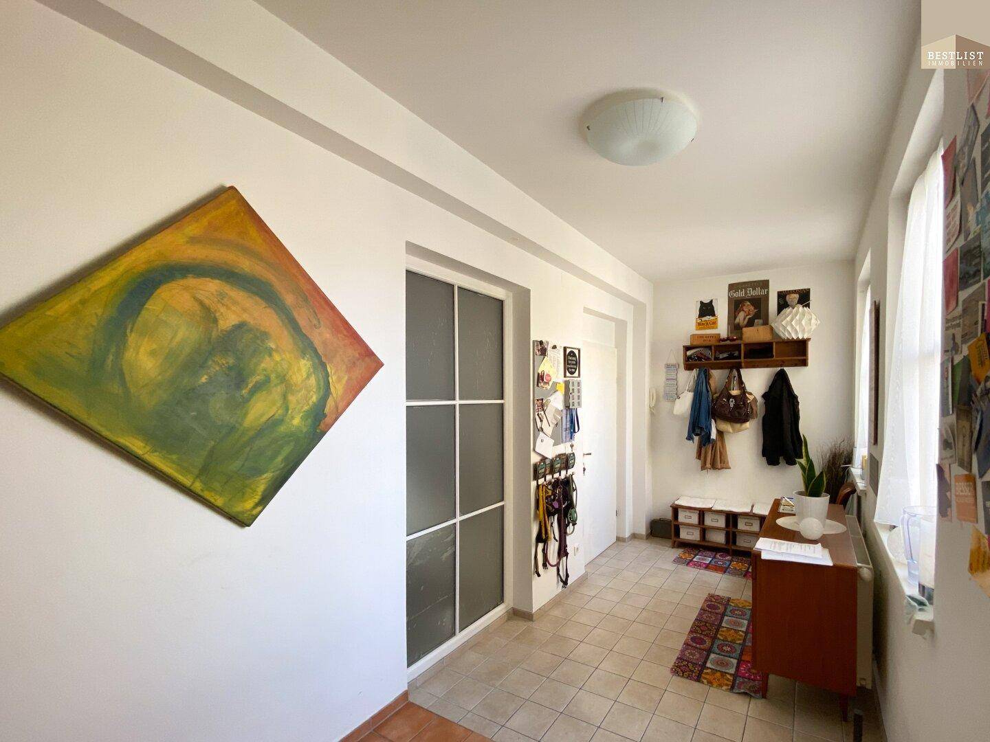 Heller Flur mit Fliesenboden, Kunstwerk und Zugang zu weiteren Räumen.