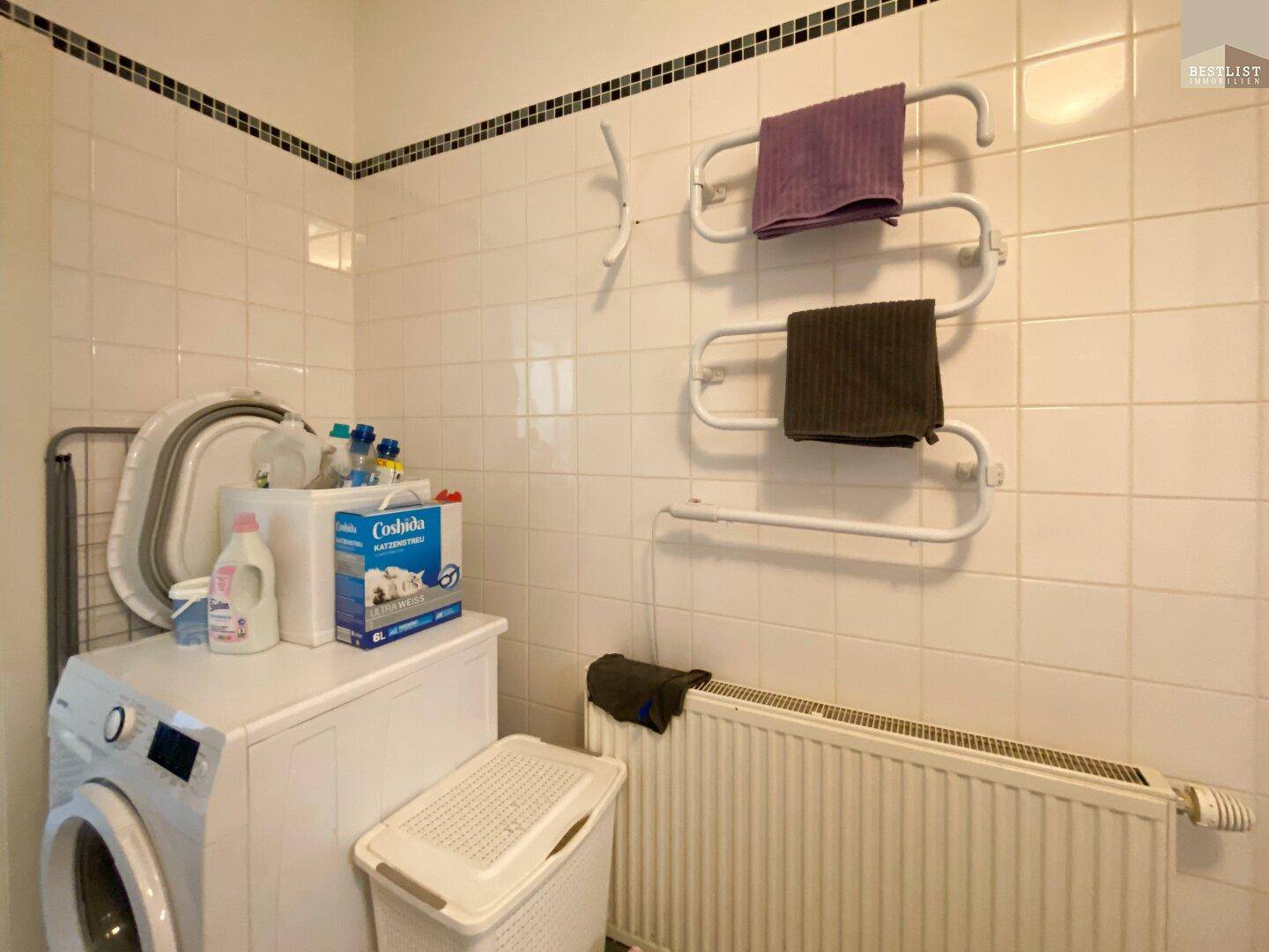 Badezimmerbereich mit Waschmaschine, Heizkörper und Handtuchhalter.