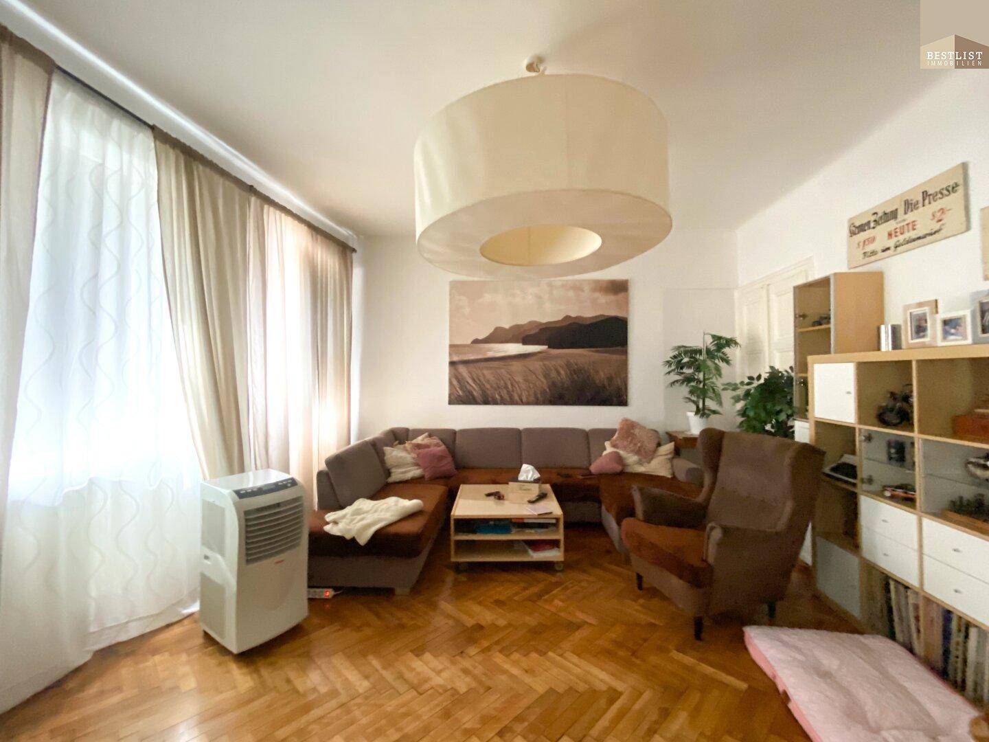 Gemütliches Wohnzimmer mit Fischgrätparkett, großem Sofa und Klimaanlage.