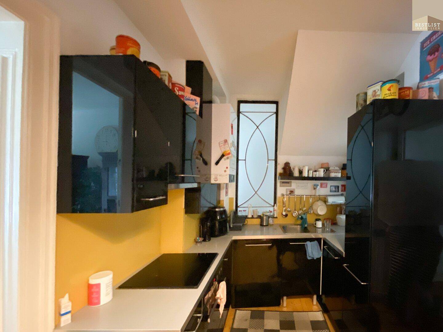 Moderne Küche mit schwarzen Hochglanzschränken, Induktionskochfeld und gelber Rückwand.