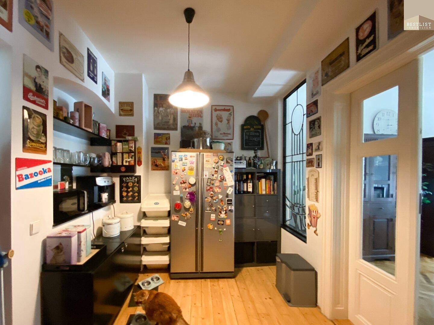 Helle Küche mit Holzboden, Kühlschrank und vielen Wanddekorationen.