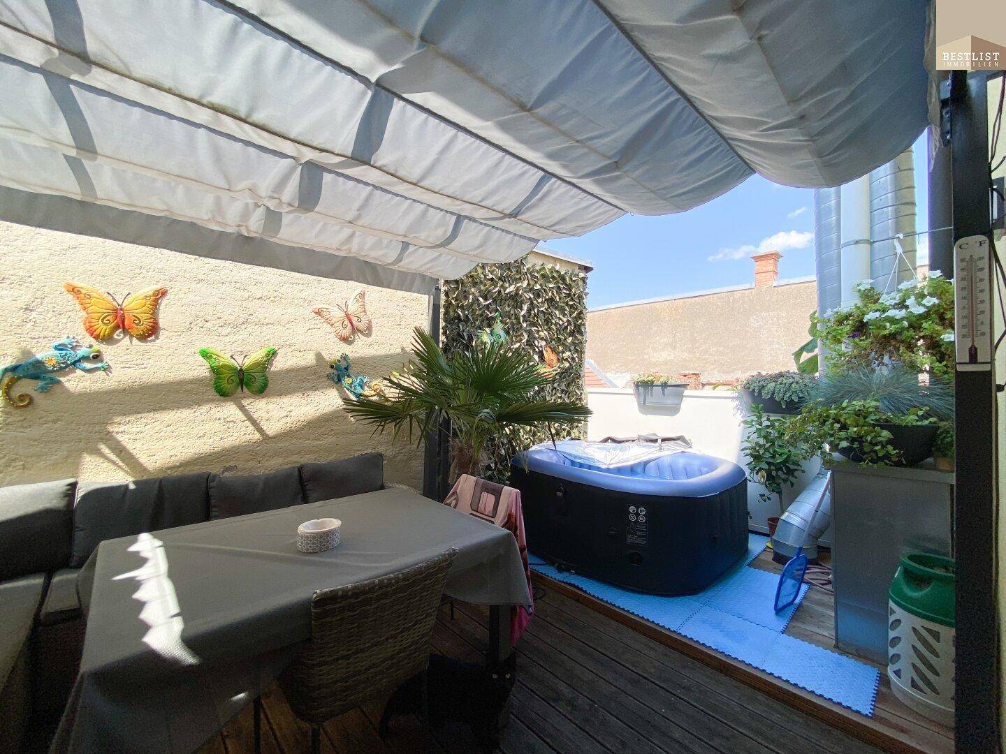 Sonnige Terrasse mit Whirlpool, Sitzbereich und Markise.