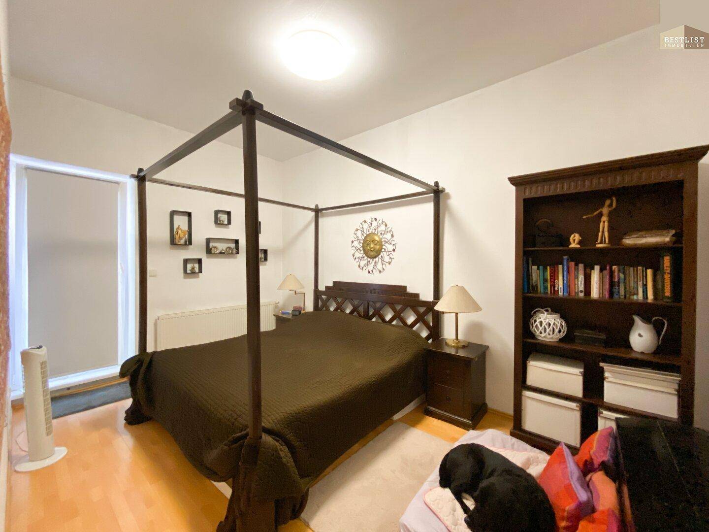 Schlafzimmer mit Himmelbett, Holzbücherregal und Parkettboden.