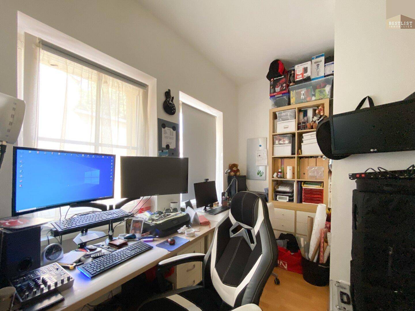 Arbeitszimmer mit mehreren Monitoren, Schreibtisch und Regalen.