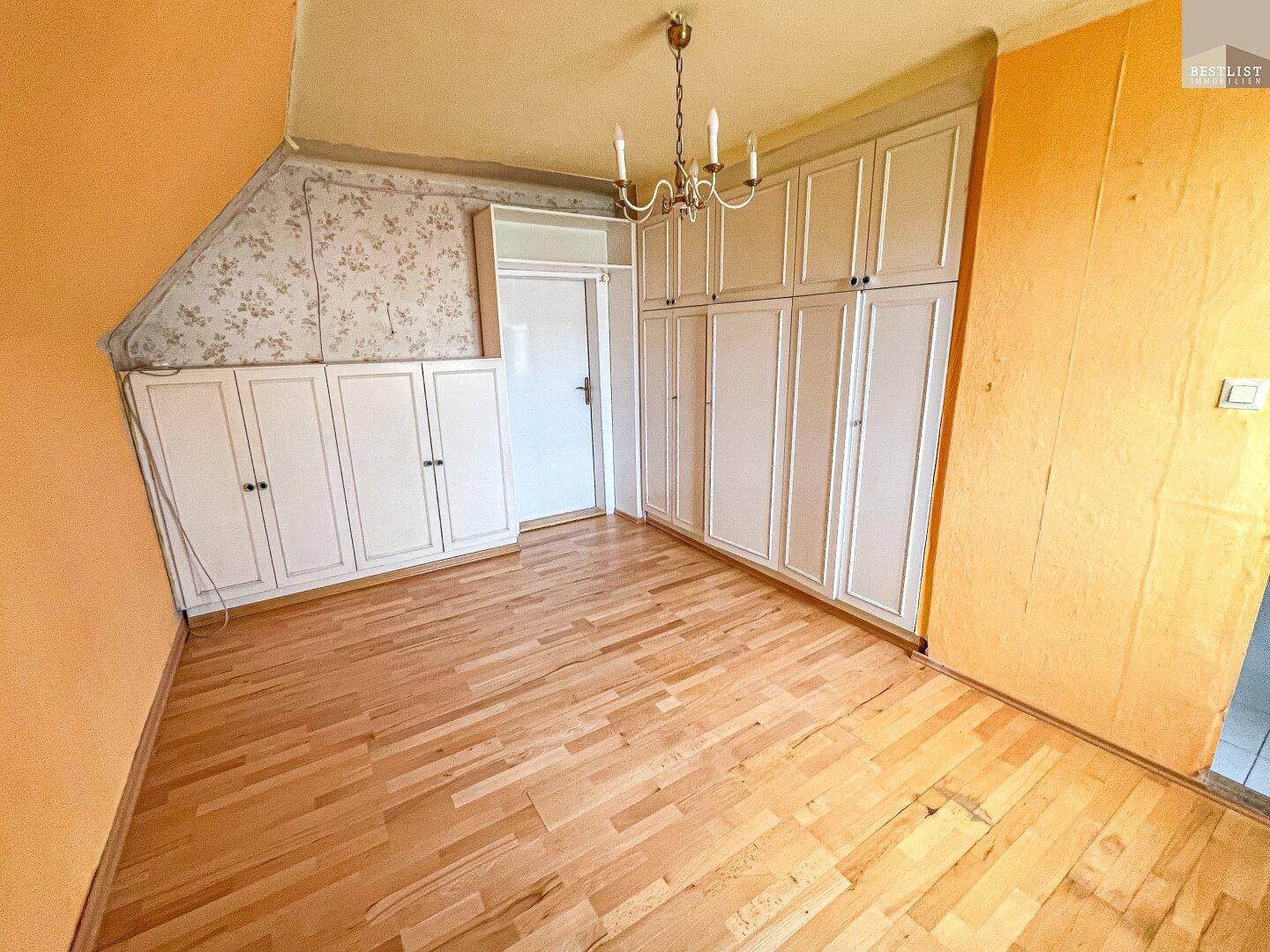 Zimmer im Dachgeschoss mit Einbauschränken, Holzboden und schräger Decke.