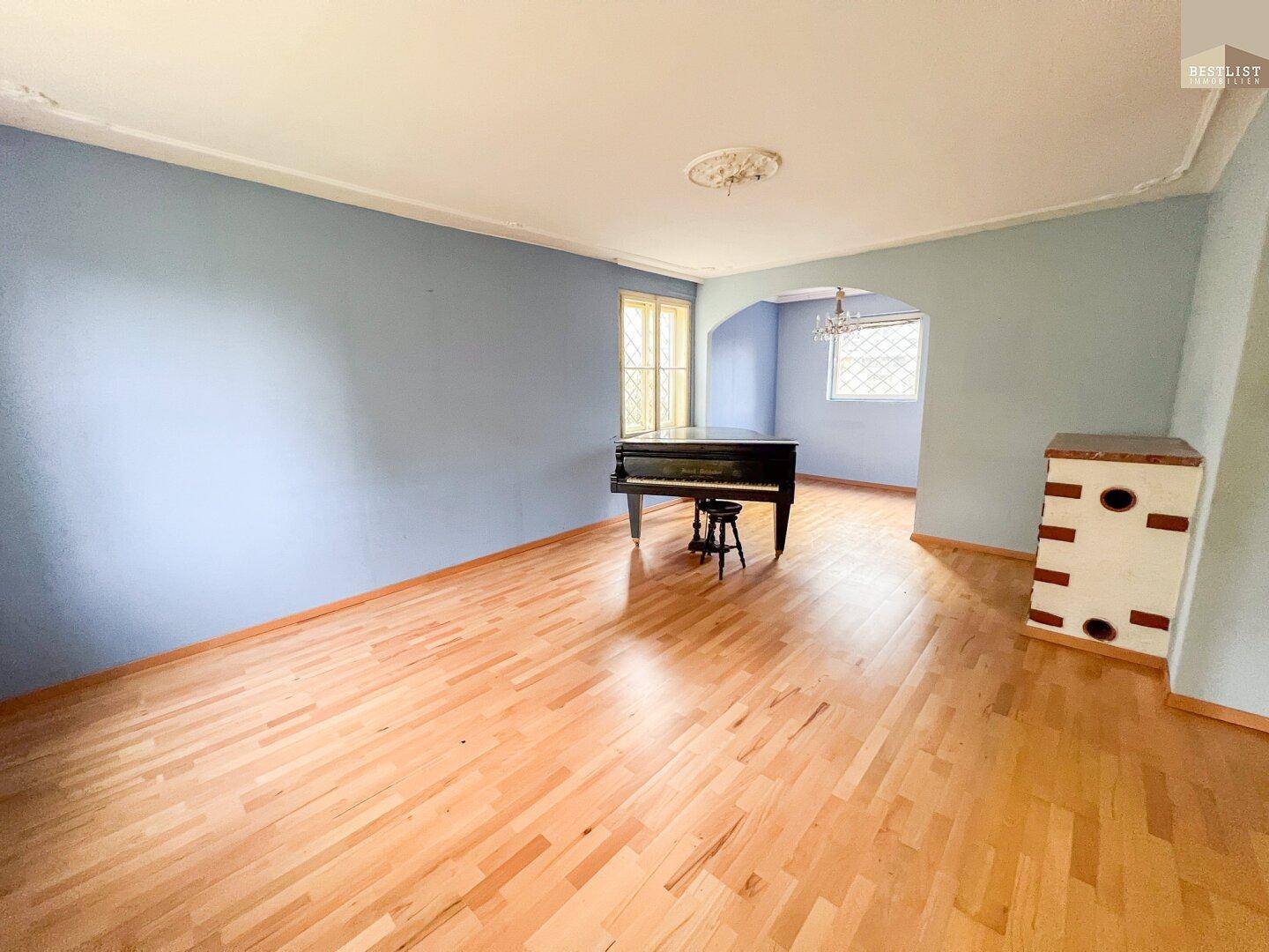 Geräumiges Wohnzimmer mit Parkettboden, blauen Wänden und einem Klavier.