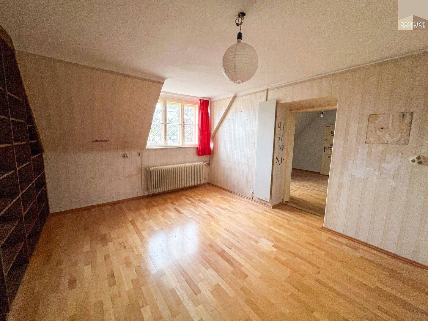 Helles Zimmer im Dachgeschoss mit Holzboden, Heizkörper und Blick nach draußen.