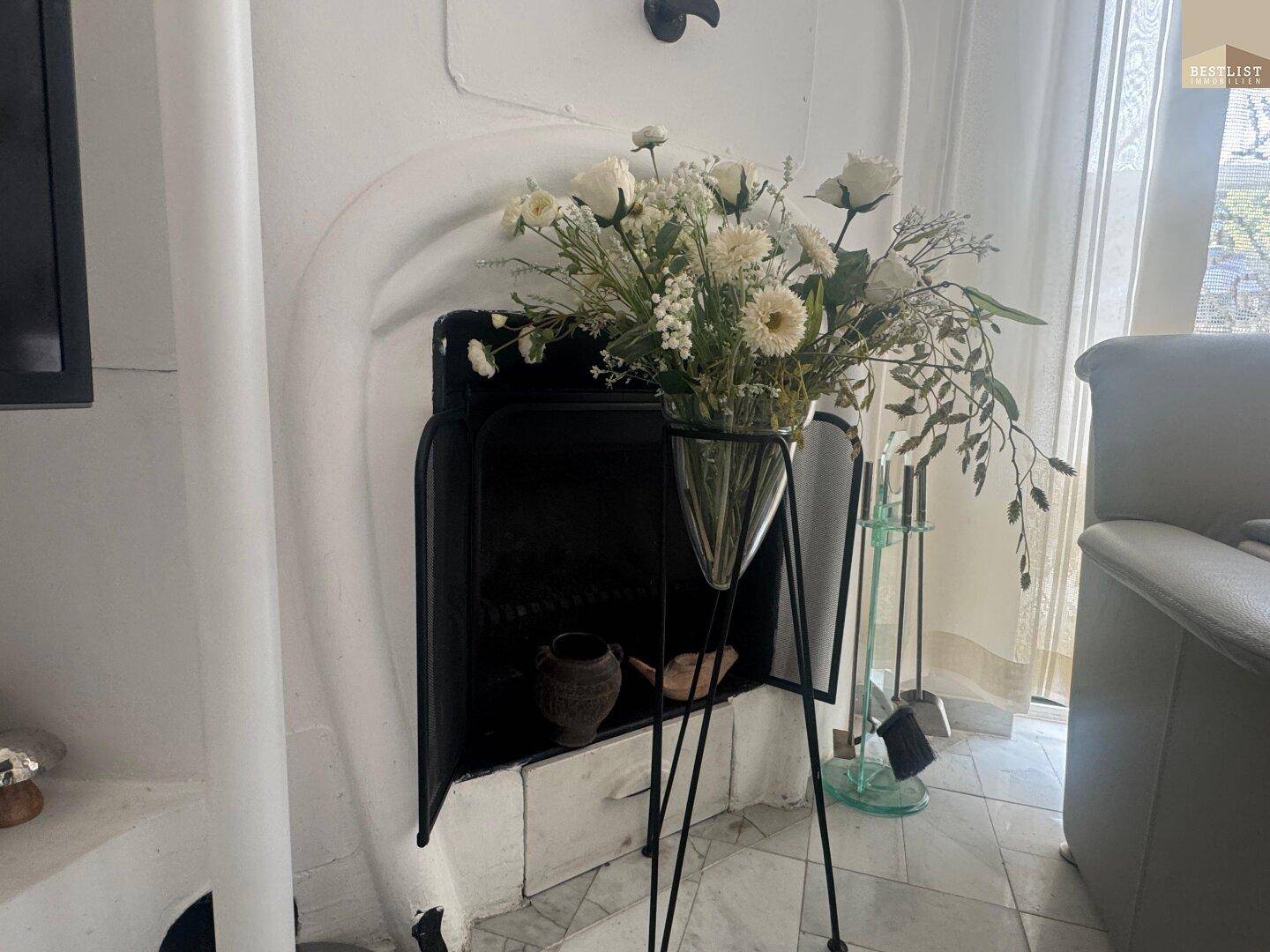 Klassischer Kamin mit weißem Putz und Blumenarrangement, der Wärme spendet.