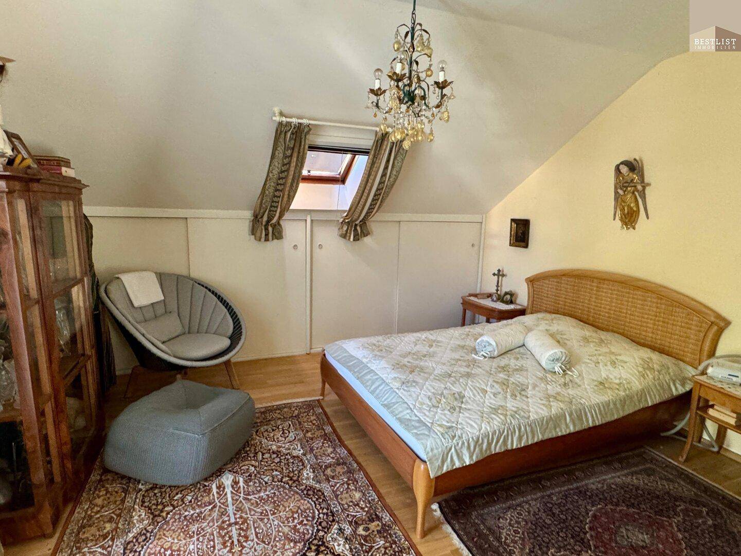 Geräumiges Schlafzimmer im Dachgeschoss mit Doppelbett, Kronleuchter und Dachfenster.