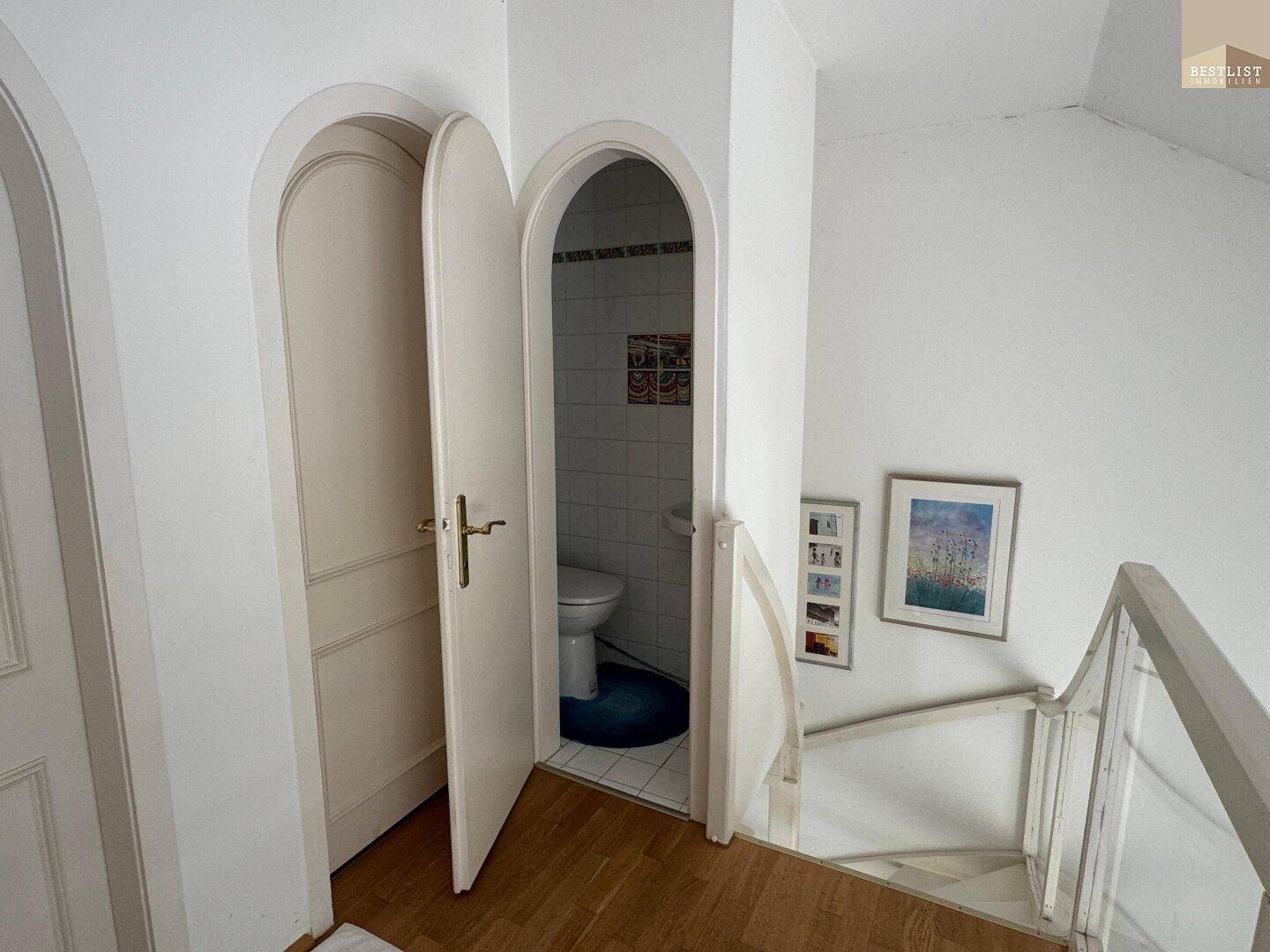 Kleines Gäste-WC mit WC und Waschbecken, zugänglich über eine Rundbogentür.