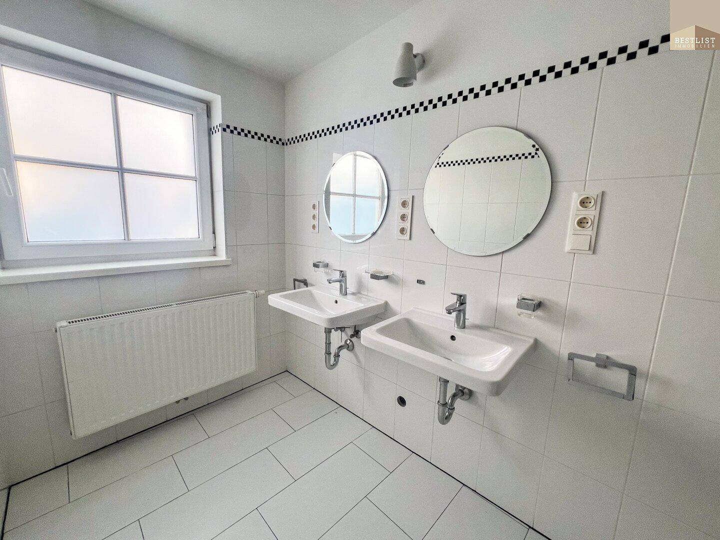 Helles Badezimmer mit Doppelwaschbecken, Fenster und weißen Fliesen.
