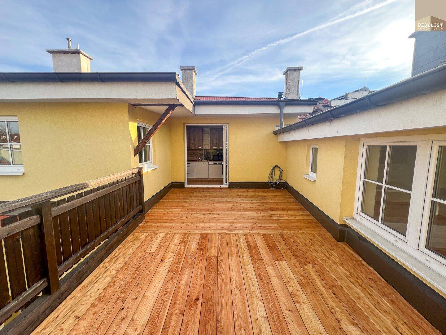 Große Holzterrasse mit Holzboden und Zugang zu einem Innenraum.