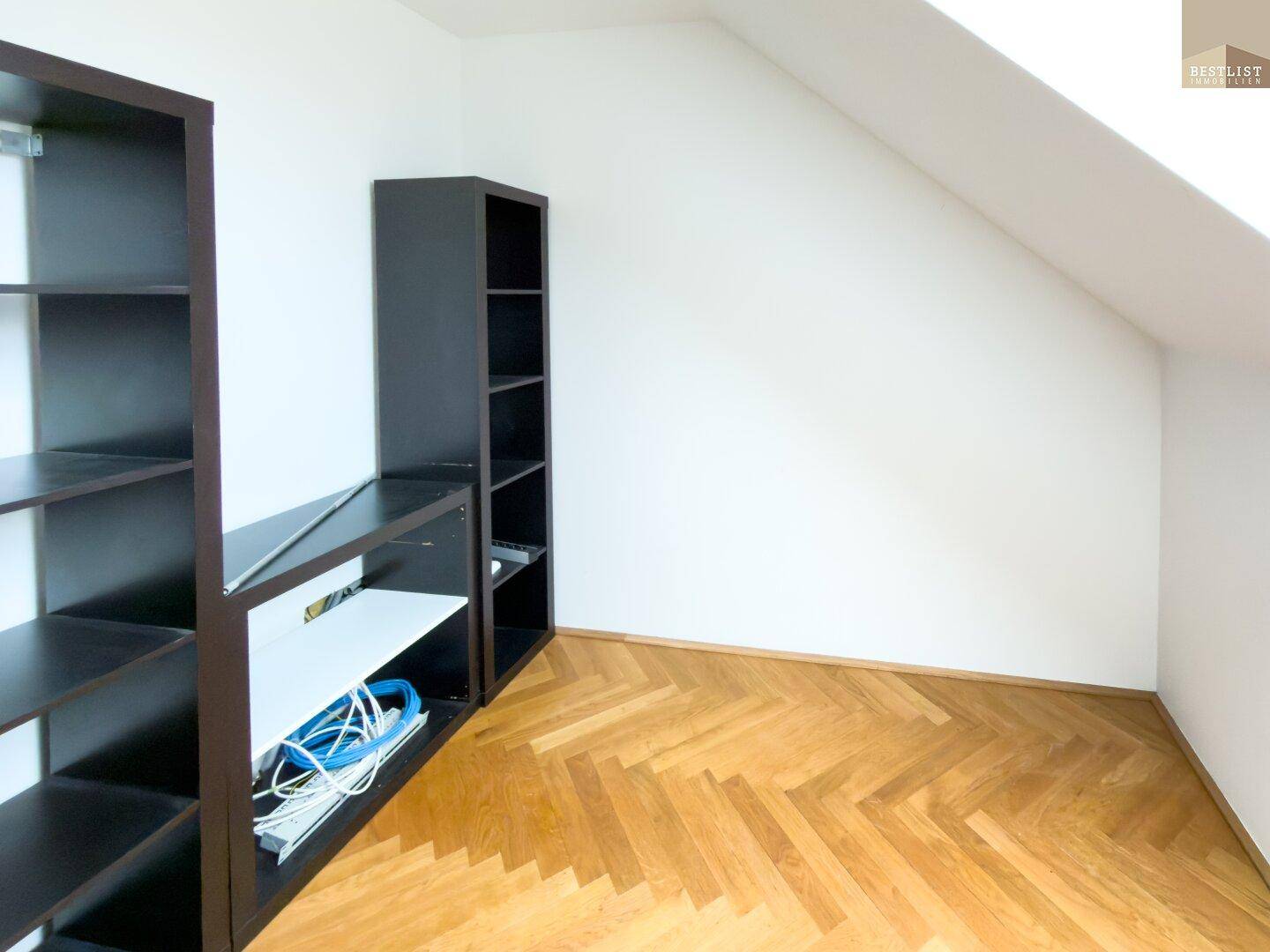 Zimmer im Dachgeschoss mit Fischgrätparkett und praktischen Regalen an der Wand.