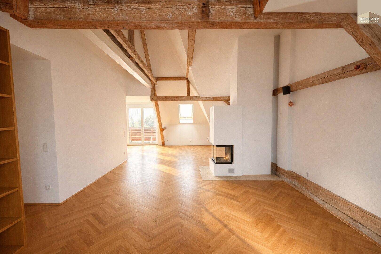 Helles Wohnzimmer im Dachgeschoss mit sichtbaren Holzbalken, Kamin und Fischgrätparkett.