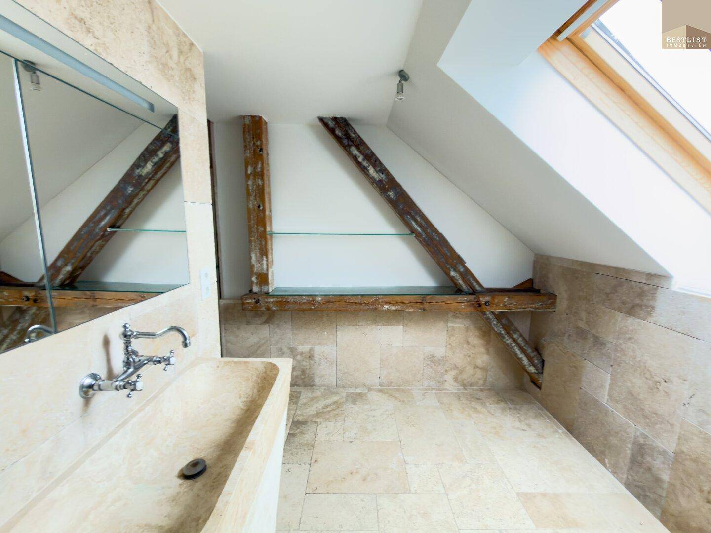 Elegantes Badezimmer im Dachgeschoss mit Natursteinfliesen, Waschtisch und Dachfenster.