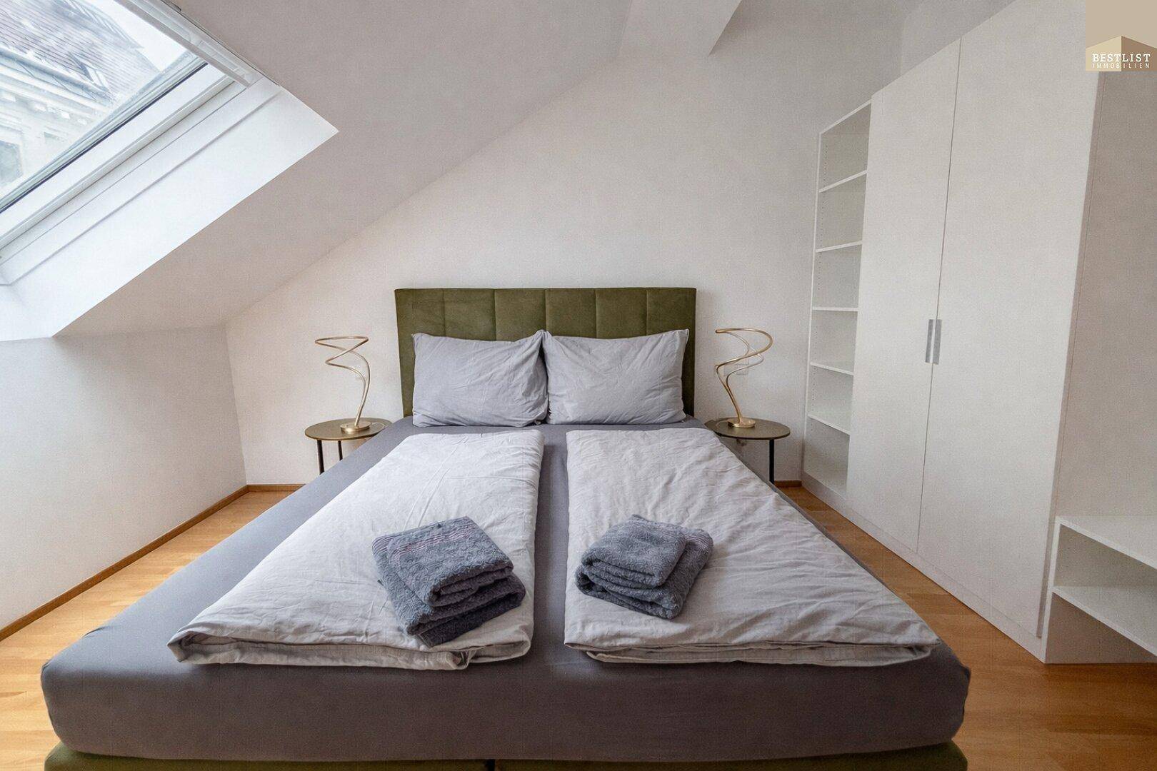 Helles Schlafzimmer mit Dachfenster, Holzboden und modernem Kleiderschrank im Dachgeschoss.