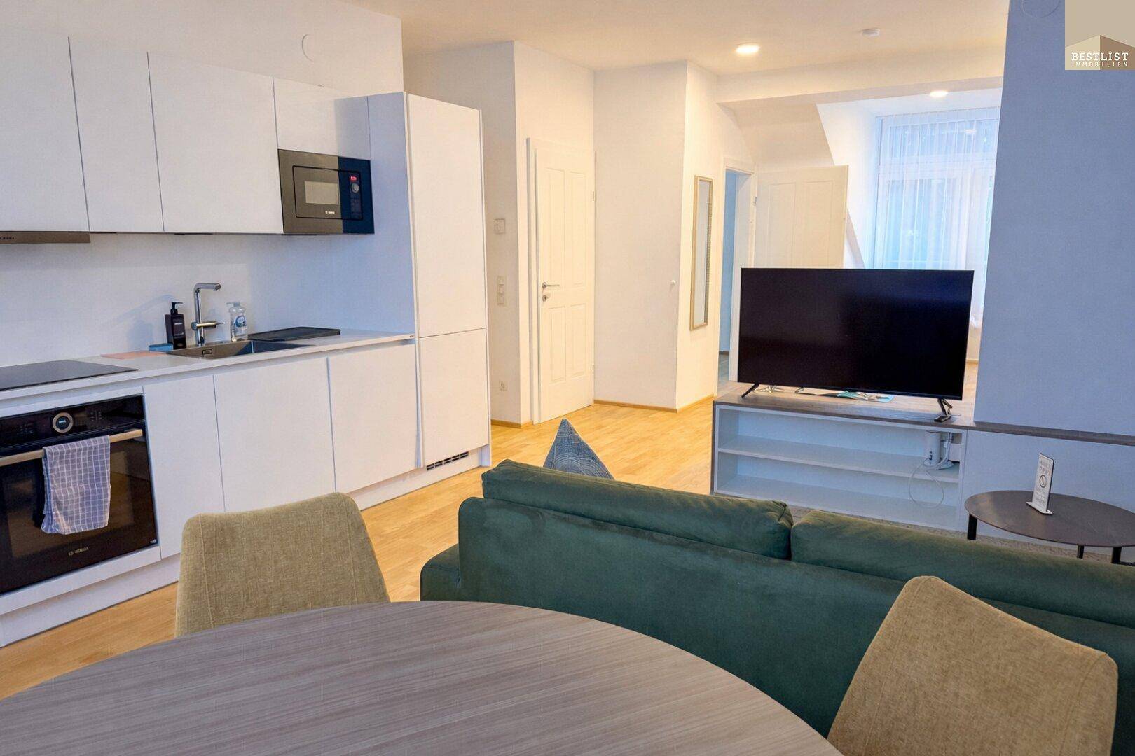 Funktionale Küche mit modernen Geräten und angrenzendem Wohnbereich mit Fernseher.