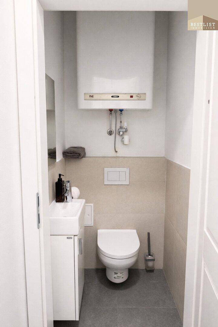 Kompaktes Gäste-WC mit wandhängender Toilette, kleinem Waschbecken und Warmwasserboiler.