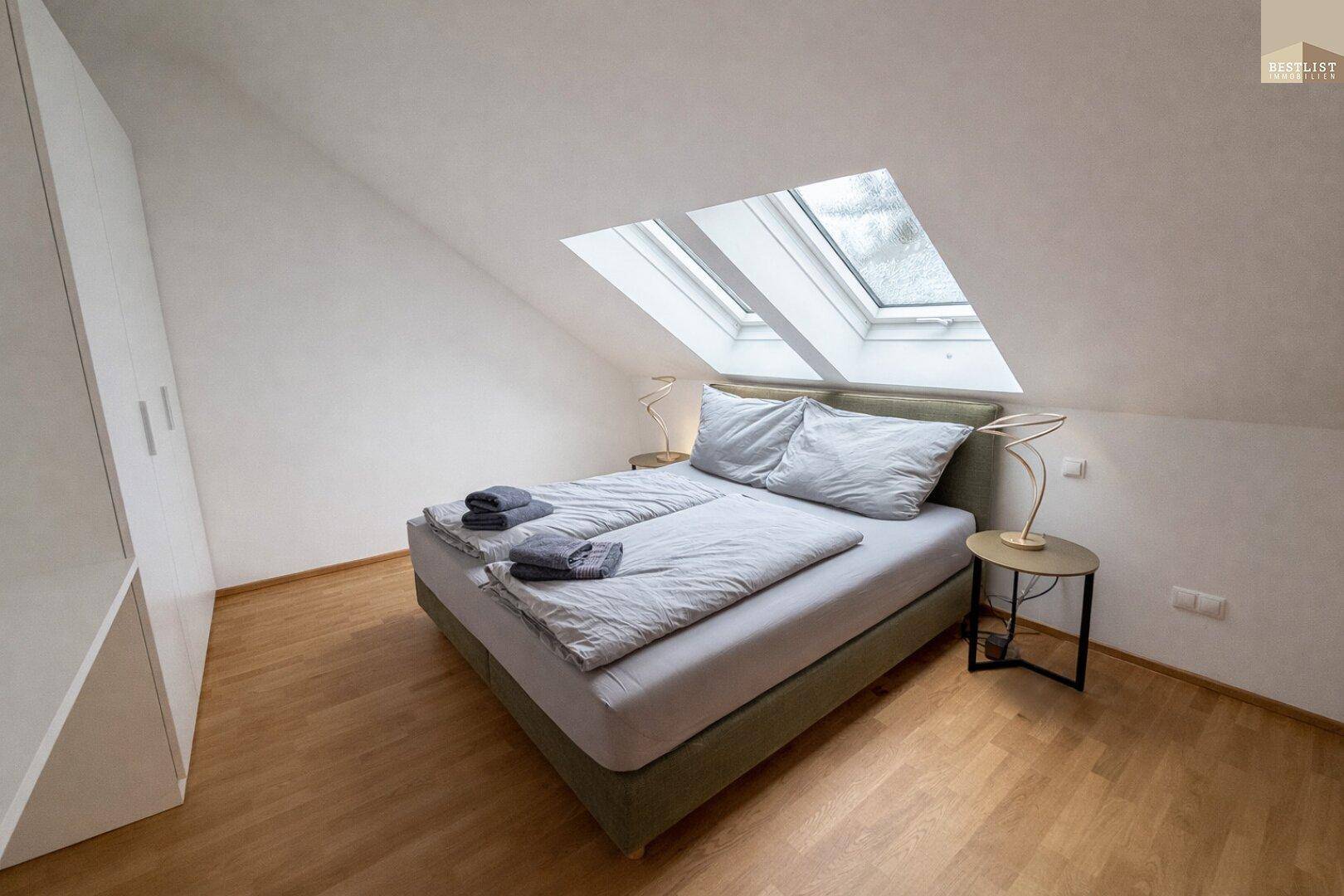 Helles Schlafzimmer im Dachgeschoss mit gemütlichem Bett, Kleiderschrank und Dachfenstern.