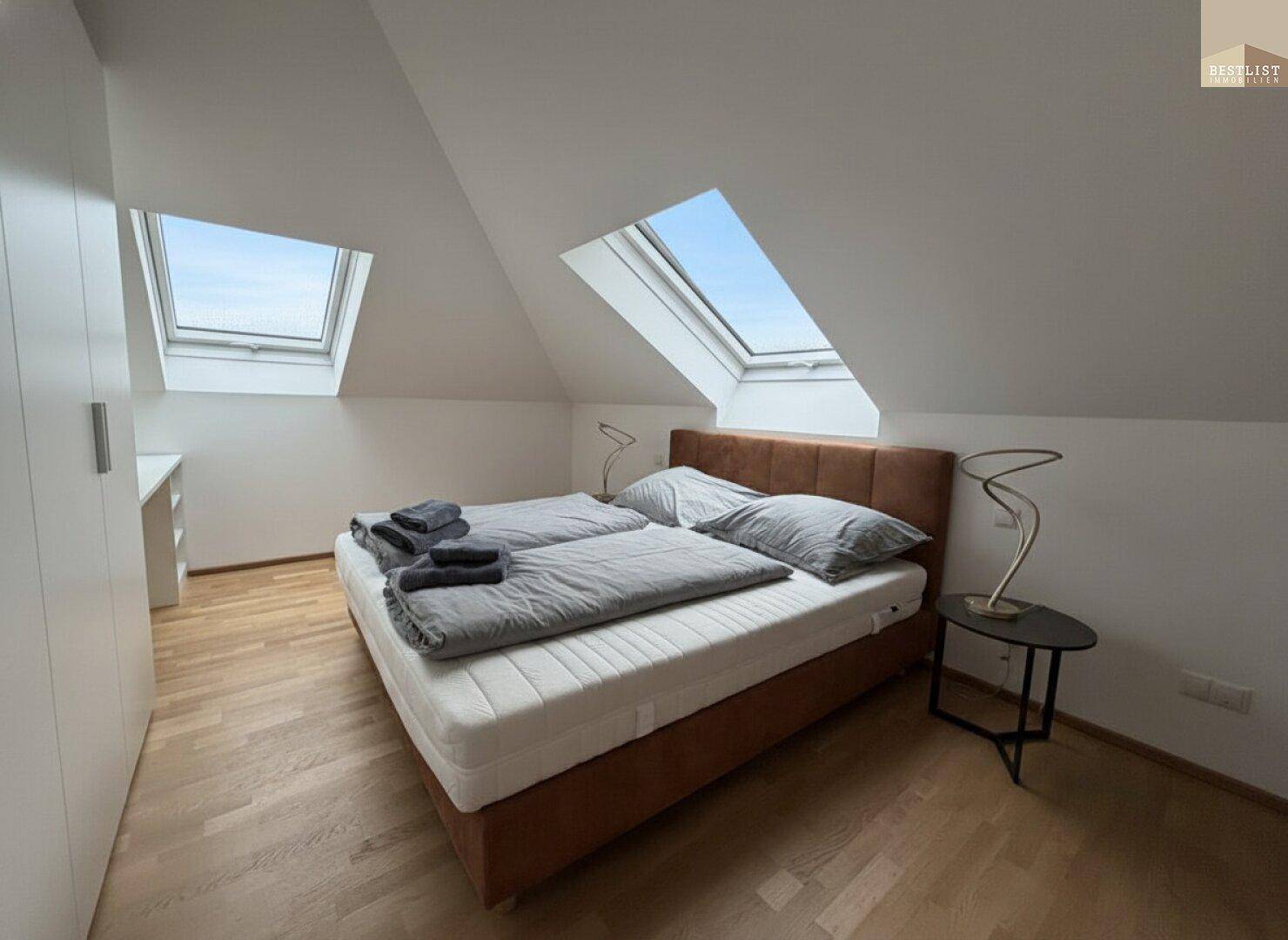 Helles Schlafzimmer im Dachgeschoss mit schrägen Wänden, Dachfenstern und Parkettboden.