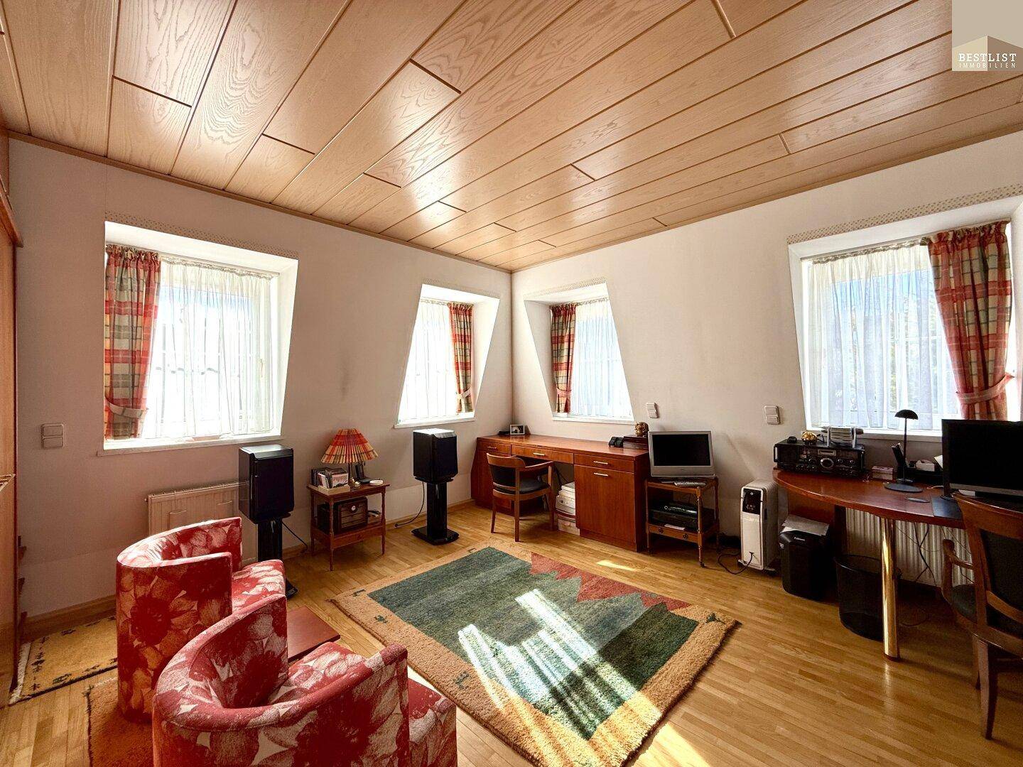 Geräumiges Schlafzimmer mit Holzdeckenverkleidung, Schreibtischen und mehreren Fenstern.