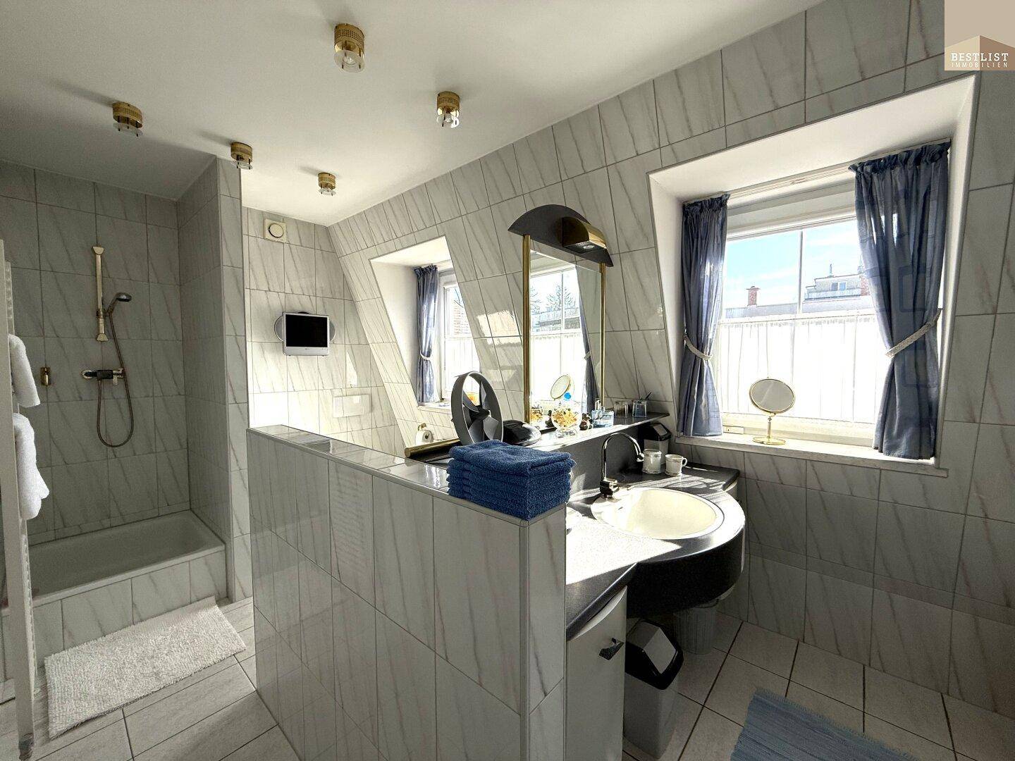 Modern gefliestes Badezimmer mit Doppelwaschbecken, Badewanne und viel Tageslicht.