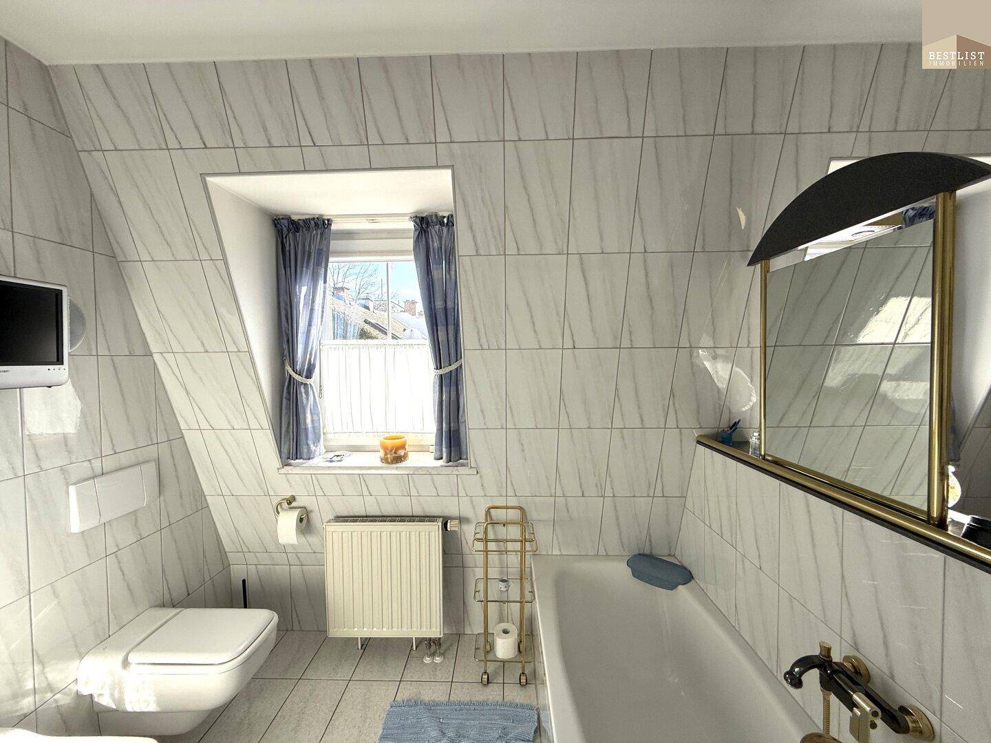 Helles Badezimmer mit Badewanne, WC und Fenster, komplett gefliest in neutralen Farben.