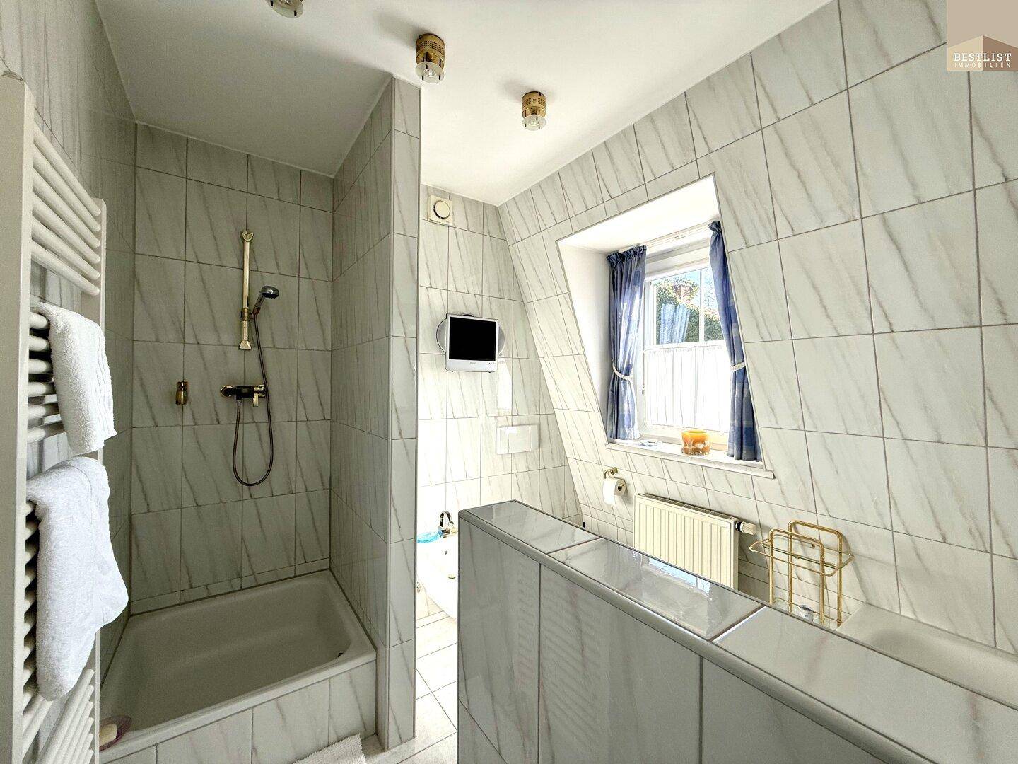 Gefliestes Badezimmer mit Badewanne, Dusche und Dachfenster, das viel Licht hereinlässt.