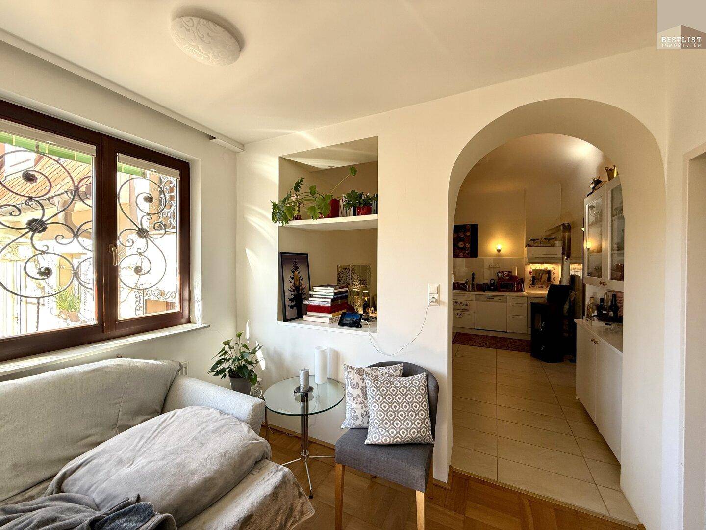 Heller Wohnbereich mit Sofa und Durchgang zu einer angrenzenden Küche, ausgestattet mit Fliesenboden.