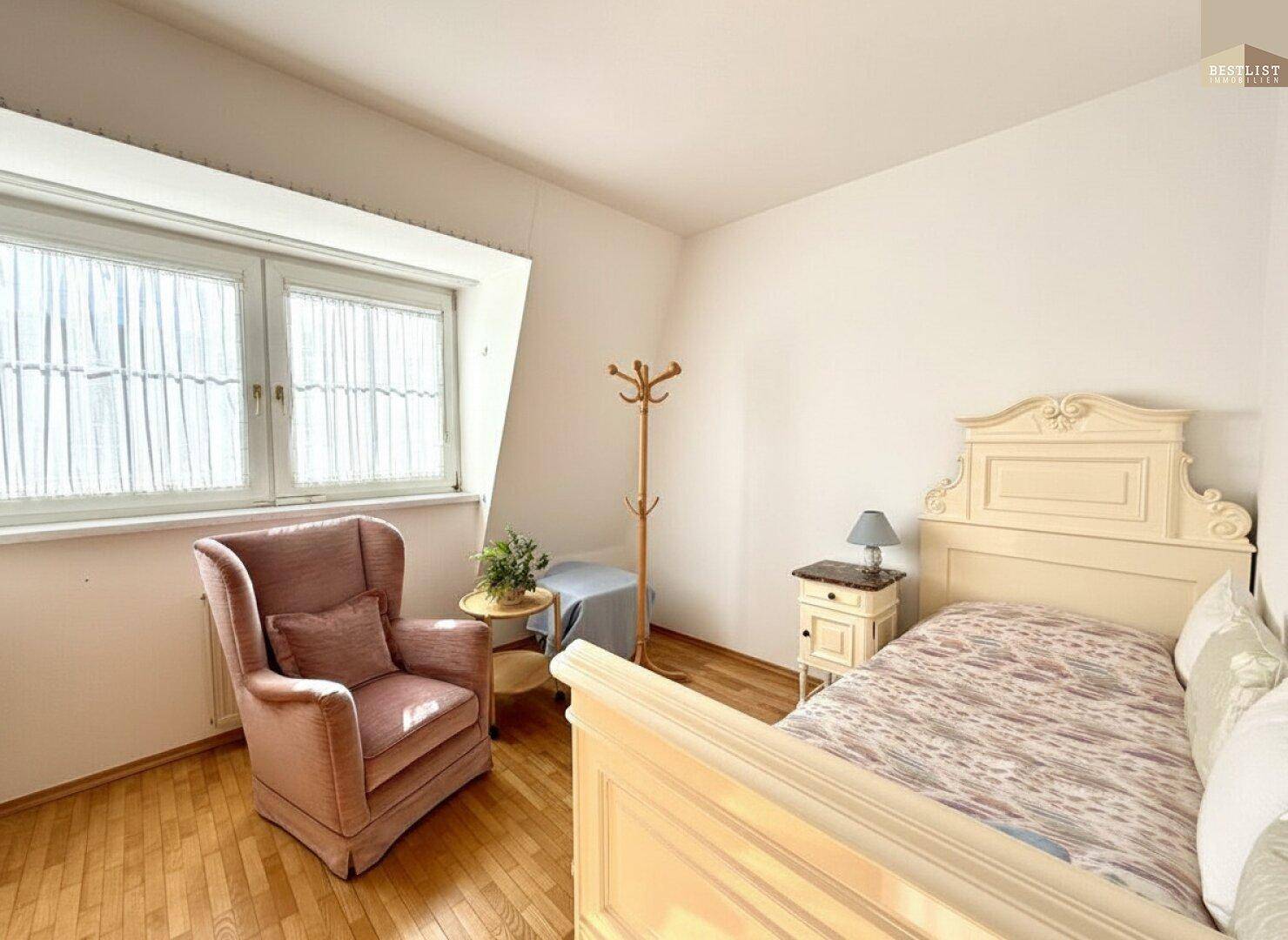 Helles Schlafzimmer mit Einzelbett, Holzfußboden und einem gemütlichen Sessel am Fenster.