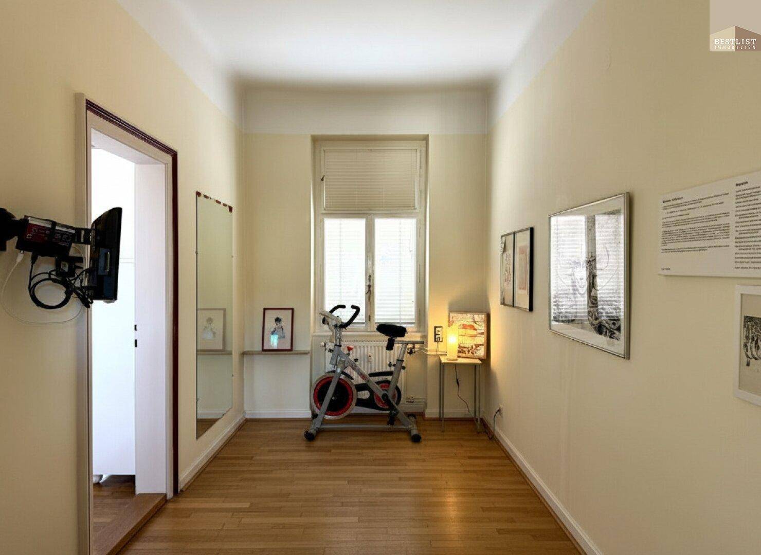 Langer Flur mit Holzboden, Fenster und einem Heimtrainer, der als Sportbereich genutzt wird.