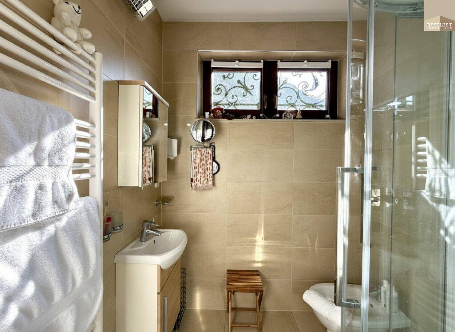 Modernes Badezimmer mit beigefarbenen Fliesen, Dusche, Bidet und Fenster für Tageslicht.